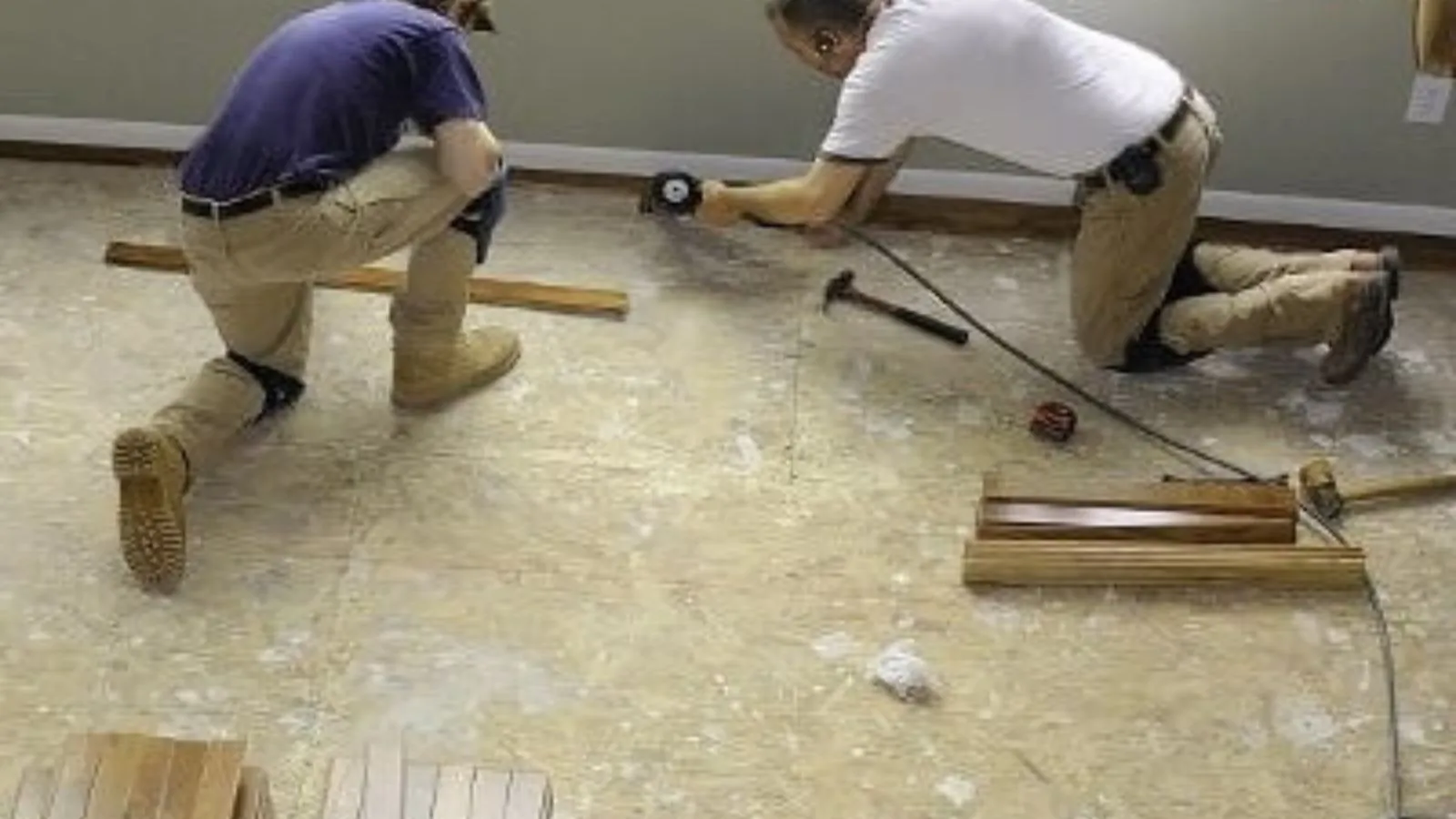 Two workers kneeling on a floor installing new flooring